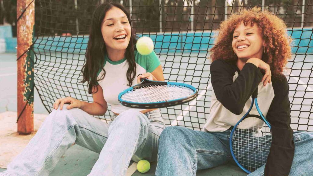 Two teens girls playing tennis outdoors at Youth Group